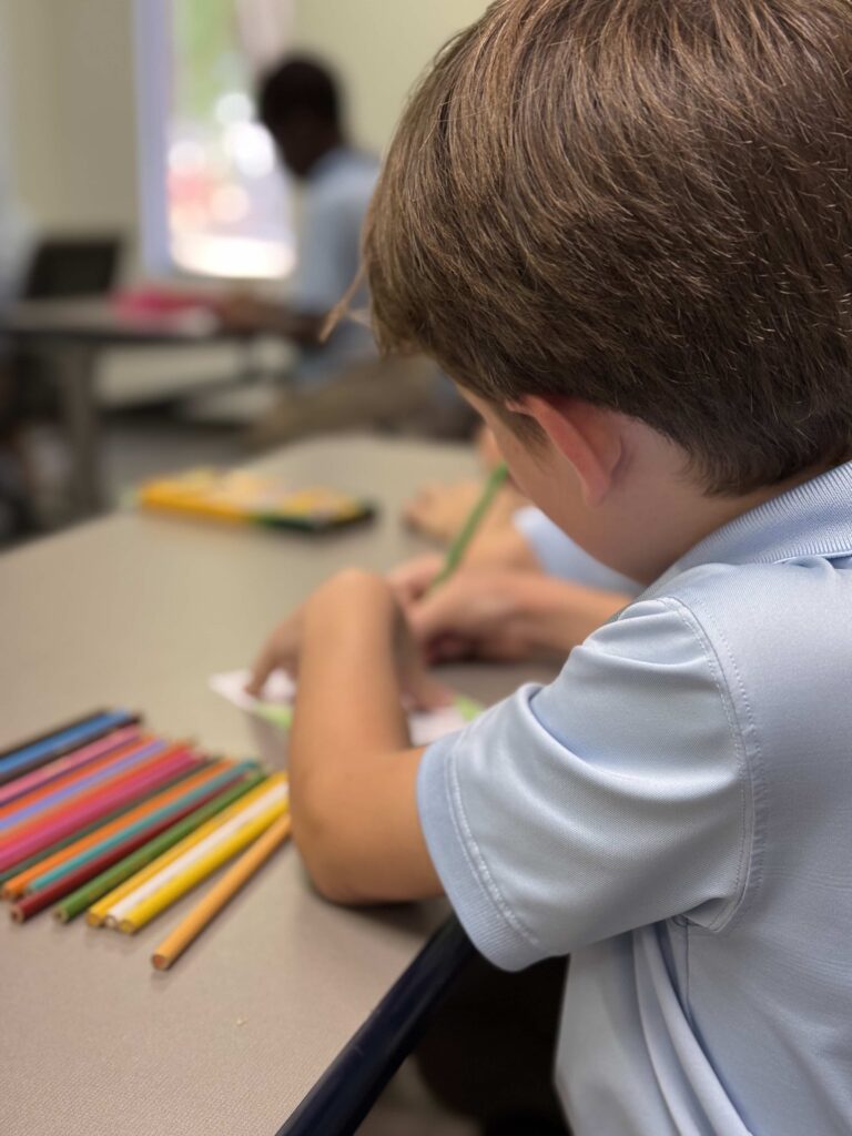 Young student in light blue shirt drawing with colored pencils at a desk