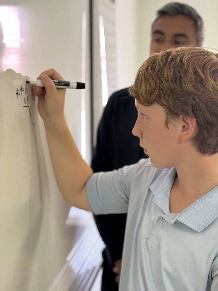 Young boy solving math problem on whiteboard with teacher watching