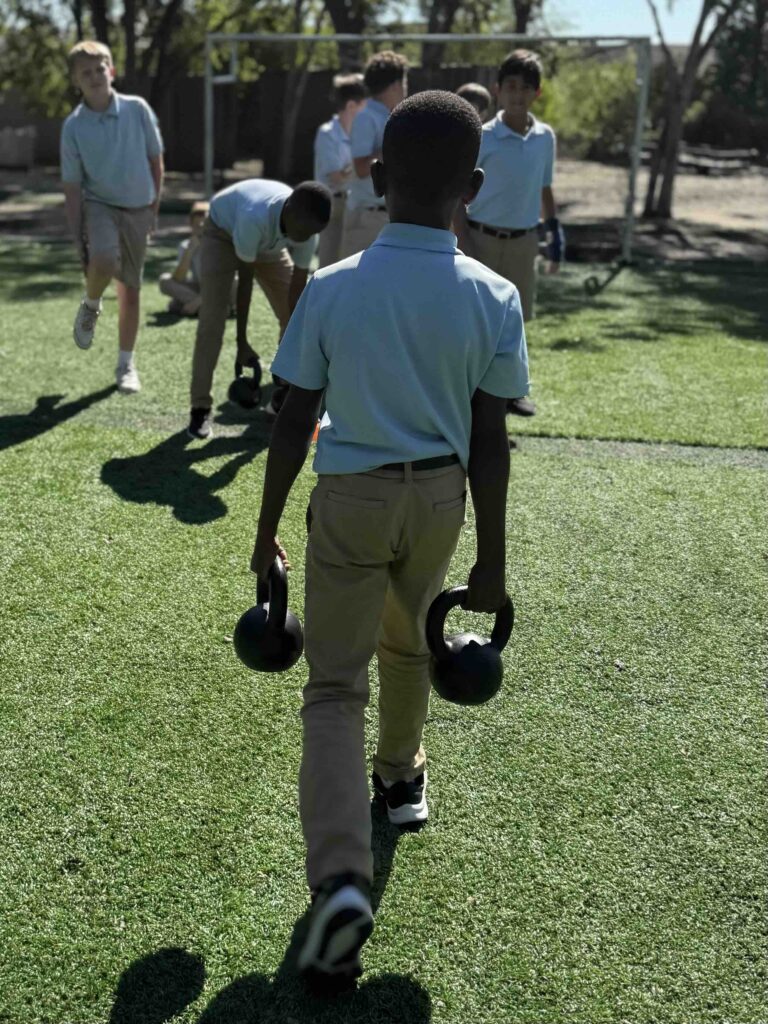 Young boys in school uniforms doing kettlebell exercises outdoors