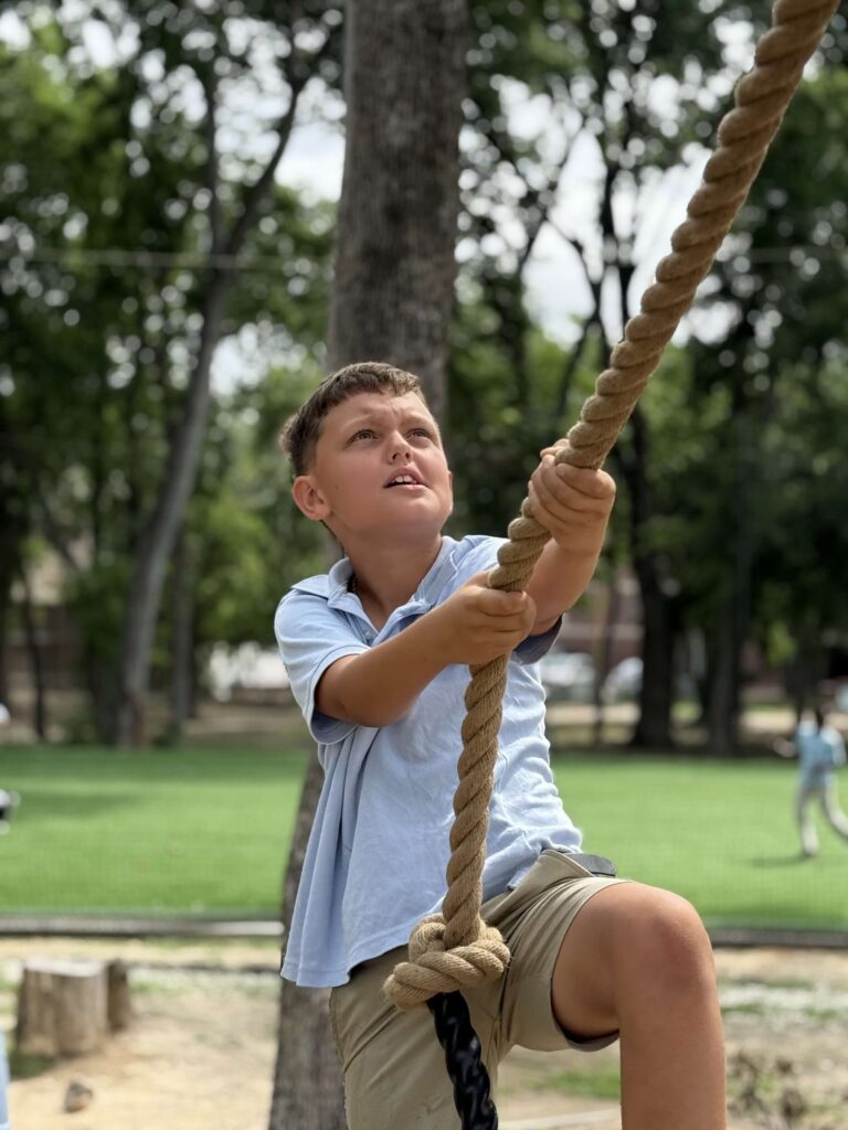 Young boy climbing a thick rope in an outdoor park